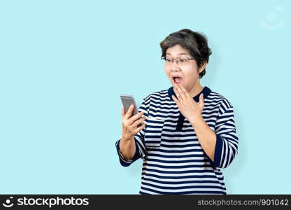 Surprised senior asian woman holding and looking smartphone on isolated background feeling surprised and amazed. Older female lifestyle concept blue background.