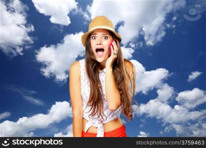 Surprised shocked emotional girl talking on mobile phone. Blue sky background.