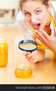 Surprised shocked mature woman female inspecting testing honey food with magnifying glass.. Woman inspecting honey with magnifying glass.