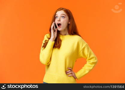 Surprised, startled good-looking redhead female hear amazing news as talking on phone, drop jaw stare left and holding smartphone near ear during conversation, standing orange background.. Surprised, startled good-looking redhead female hear amazing news as talking on phone, drop jaw stare left and holding smartphone near ear during conversation, standing orange background