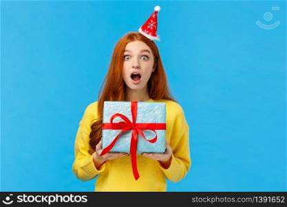Surprised startled pretty redhead girl receive unexpected gift for christmas classmate, open mouth astonished and speechless staring camera as holding cute blue present wrapped box, studio background.. Surprised startled pretty redhead girl receive unexpected gift for christmas classmate, open mouth astonished and speechless staring camera as holding cute blue present wrapped box, studio background