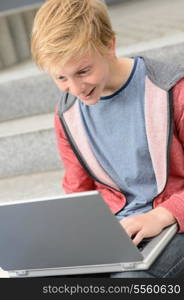 Surprised teenage student boy using laptop sitting outside on steps