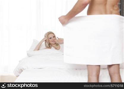 Surprised woman looking at nude man holding towel in bedroom