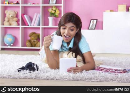Surprised woman using digital tablet while drinking coffee at home