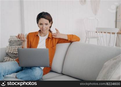 Surprised woman using laptop, sitting on couch at home. Amazed female looking at computer screen, chatting online in social network, making video call, reading email, astonished with good news.. Surprised girl chatting by video call at laptop, astonished with good news, sitting on couch at home