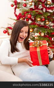 Surprised woman with Christmas gift in front of tree