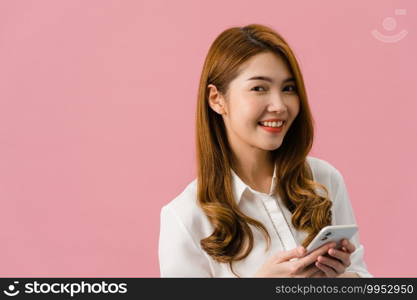 Surprised young Asia lady using mobile phone with positive expression, smiles broadly, dressed in casual clothing and looking at camera on pink background. Happy adorable glad woman rejoices success.
