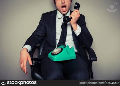 Surprised young businessman in office chair is on the phone