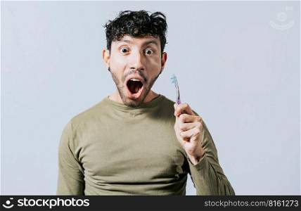 Surprised young man holding a toothbrush. Amazed teenager holding toothbrush isolated, Guy holding toothbrush with amazed face isolated on white