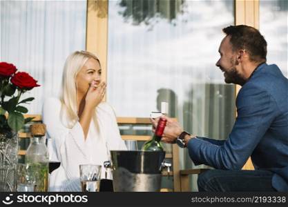 surprised young woman looking man giving engagement ring restaurant