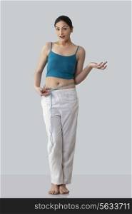 Surprised young woman measuring waist isolated over gray background