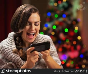 Surprised young woman reading sms near christmas tree