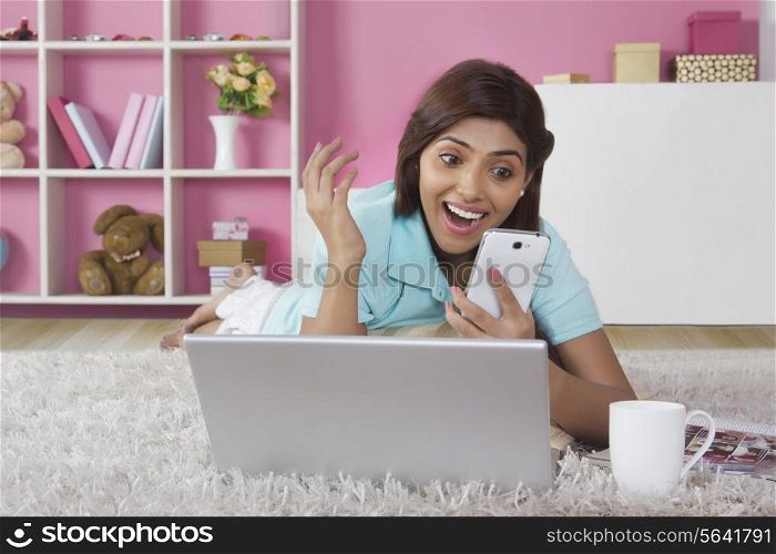 Surprised young woman reading text message on mobile phone at home