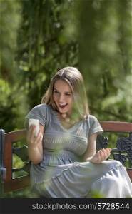 Surprised young woman reading text message on smart phone in park