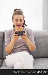 Surprised young woman sitting on sofa and reading sms