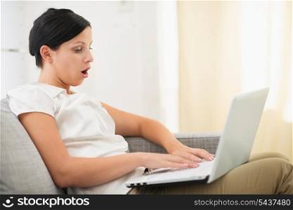 Surprised young woman using laptop in living room