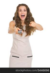 Surprised young woman with tv remote control pointing in camera