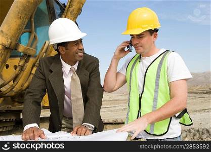 Surveyor and construction worker studying blueprint