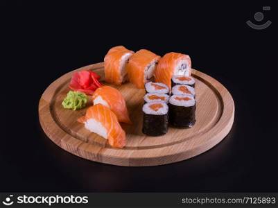 sushi and rolls on a wooden, round board, side view on a black background. tasty rolls on the board