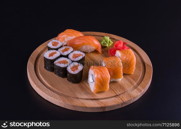 sushi and rolls on a wooden, round board, side view on a black background. tasty rolls on the board