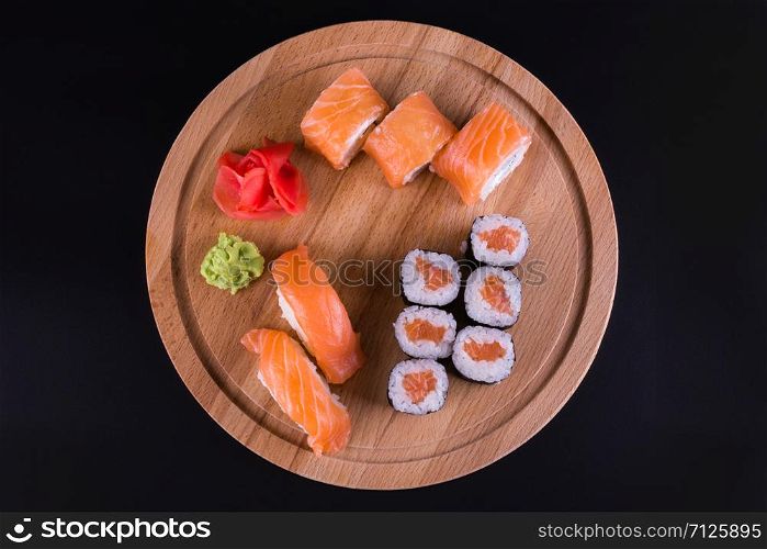 sushi and rolls on a wooden round board, top view on a black background. tasty rolls on the board