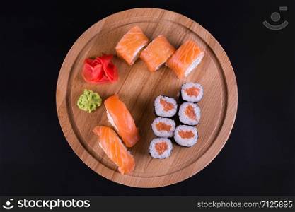 sushi and rolls on a wooden round board, top view on a black background. tasty rolls on the board