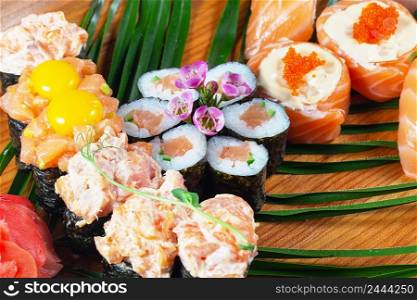 Sushi and rolls with sauce and raw quail eggs on a wooden plate with green leaves. Close-up. Selective focus. Traditional oriental dish. Sushi and rolls with sauce and raw quail eggs on wooden plate with green leaves