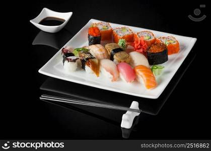 sushi in a white plate with sauce pot and chopsticks on a black background with reflection . sushi in a plate on a black background