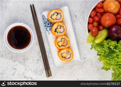 Sushi is in a plate with chopsticks and dipping sauce on a white cement floor.