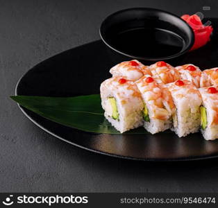 Sushi roll covered with shrimp meat on black ceramic plate