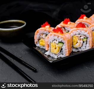 Sushi roll with fried salmon on black plate