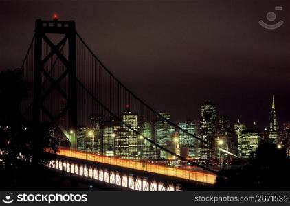 Suspension bridge at night with glowing urban cityscape in background