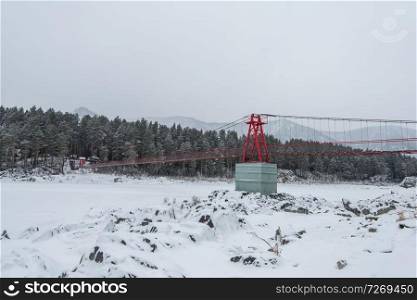 Suspension hanging bridge above winter frozen mountain Katun river, Altai mountains, Siberia, Russia. Suspension hanging bridge above winter frozen river