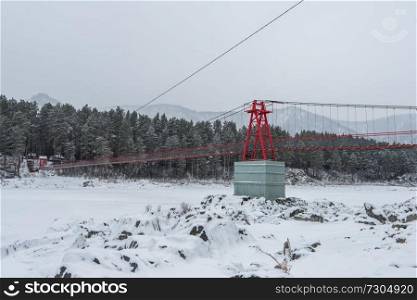 Suspension hanging bridge above winter frozen mountain Katun river, Altai mountains, Siberia, Russia. Suspension hanging bridge above winter frozen river