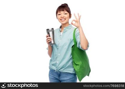 sustainability and people concept - asian woman in turquoise shirt with thermo cup and green reusable bag for food shopping showing ok gesture over white background. woman with tumbler and reusable food shopping bag