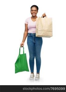 sustainability and people concept - happy smiling young african american woman comparing green reusable canvas bag for food shopping with paper bag over white background. woman comparing reusable and paper bags