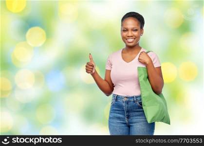 sustainability and people concept - happy smiling young african american woman with reusable canvas bag for food shopping over lights on green background. woman with reusable canvas bag for food shopping