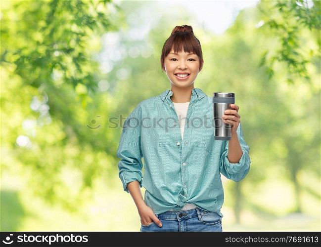 sustainability and people concept - portrait of asian woman in turquoise shirt with thermo cup or tumbler for hot drinks over green natural background. woman with thermo cup or tumbler for hot drinks