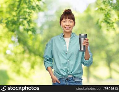 sustainability and people concept - portrait of asian woman in turquoise shirt with thermo cup or tumbler for hot drinks over green natural background. woman with thermo cup or tumbler for hot drinks