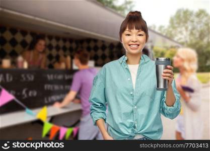sustainability and people concept - portrait of young asian woman in turquoise shirt with thermo cup or tumbler for hot drinks over food truck background. woman with thermo cup or tumbler over food truck