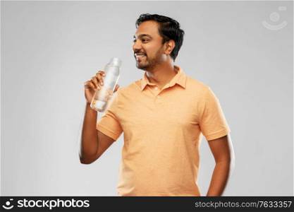 sustainability, consumerism and eco friendly concept - happy smiling indian man drinking water from reusable glass bottle grey background. happy indian man drinking water from glass bottle