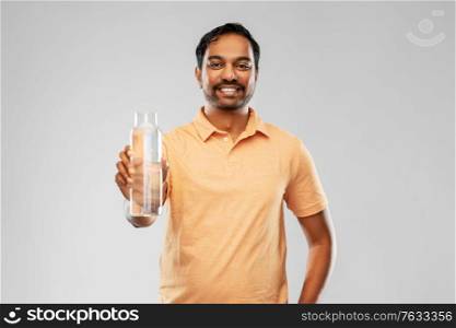 sustainability, consumerism and eco friendly concept - happy smiling indian man showing water in reusable glass bottle grey background. happy indian man showing water in glass bottle