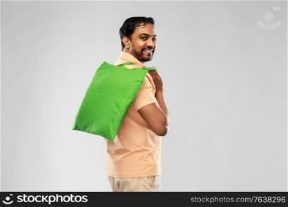 sustainability, consumerism and eco friendly concept - happy smiling indian man with green reusable canvas bag for food shopping on grey background. man with reusable canvas bag for food shopping