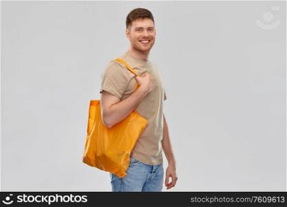 sustainability, consumerism and eco friendly concept - happy smiling man with reusable canvas bag for food shopping on grey background. man with reusable canvas bag for food shopping
