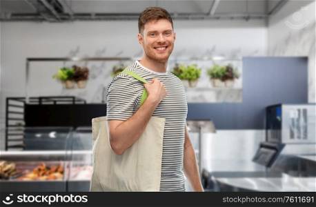 sustainability, consumerism and eco friendly concept - happy smiling man with reusable canvas bag for food shopping over store background. man with reusable canvas bag for food shopping