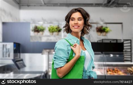 sustainability, eco and green living concept - portrait of happy smiling young woman in turquoise shirt with reusable canvas bag for food shopping over supermarket or grocery store background. woman with reusable canvas bag for food shopping