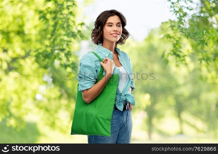sustainability, eco living and people concept - portrait of happy smiling young woman in turquoise shirt with green reusable canvas bag for food shopping over green natural background. woman with reusable canvas bag for food shopping