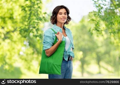 sustainability, eco living and people concept - portrait of happy smiling young woman in turquoise shirt with green reusable canvas bag for food shopping over green natural background. woman with reusable canvas bag for food shopping