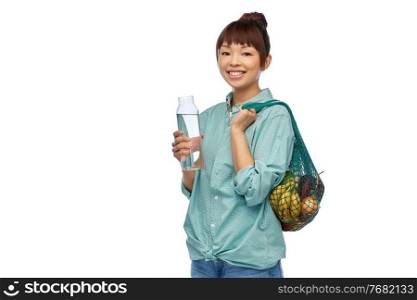 sustainability, eco living and people concept - portrait of happy smiling young asian woman with green reusable string bag for food shopping and glass bottle of water over white background. woman with food in string bag and glass bottle