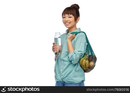 sustainability, eco living and people concept - portrait of happy smiling young asian woman with green reusable string bag for food shopping and glass bottle of water over white background. woman with food in string bag and glass bottle